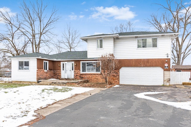 view of front of house featuring driveway, a garage, roof with shingles, fence, and brick siding