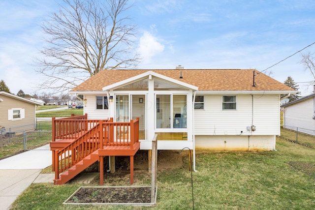 rear view of house with a shingled roof, a lawn, fence, and a sunroom