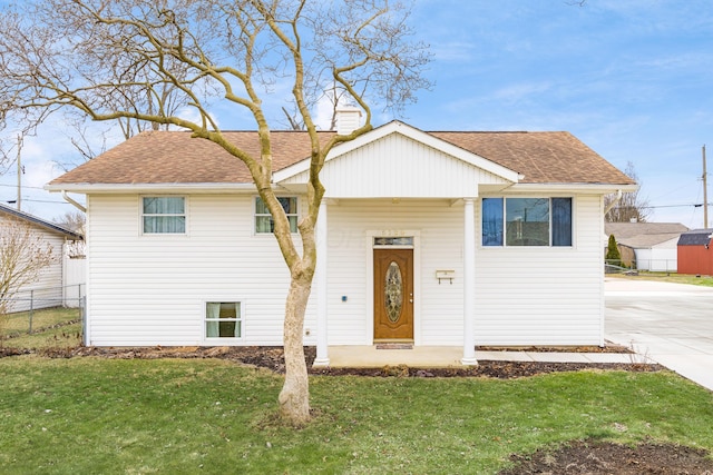 raised ranch featuring a chimney, fence, a front lawn, and roof with shingles