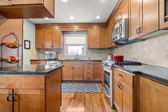 kitchen featuring brown cabinets, a sink, stainless steel appliances, light wood-style floors, and backsplash