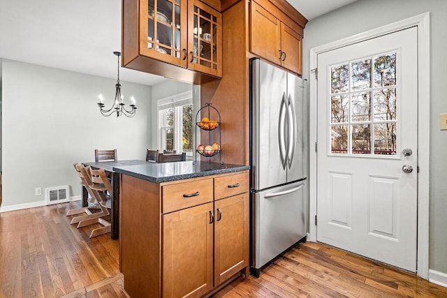 kitchen featuring stainless steel fridge, visible vents, brown cabinetry, light wood-style flooring, and glass insert cabinets