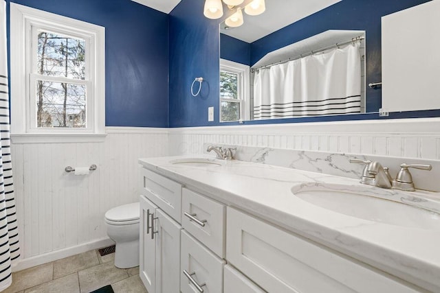 bathroom with toilet, a wainscoted wall, double vanity, and a sink