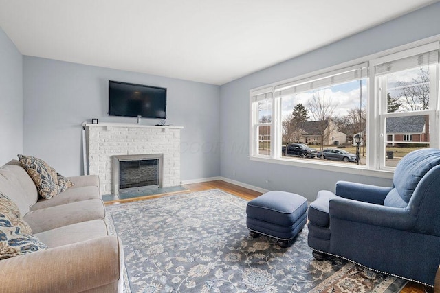 living room with a brick fireplace, baseboards, and wood finished floors