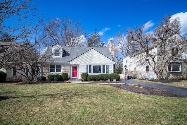 cape cod house featuring driveway, stone siding, a chimney, and a front lawn