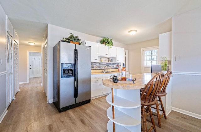 kitchen with tasteful backsplash, stainless steel fridge with ice dispenser, light countertops, open shelves, and a sink