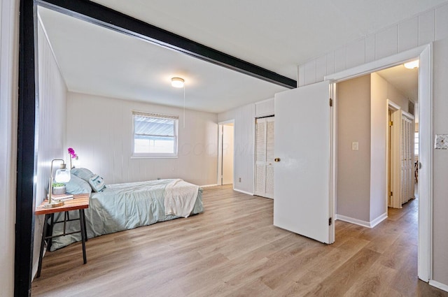 bedroom with beam ceiling, light wood-style flooring, and baseboards