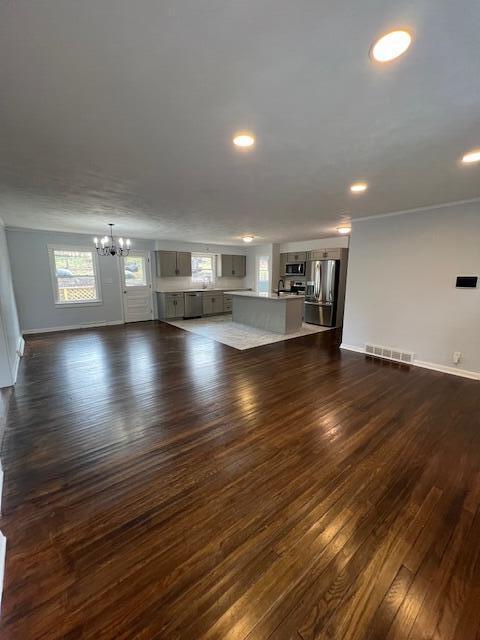 unfurnished living room featuring visible vents, baseboards, dark wood-style floors, a notable chandelier, and recessed lighting