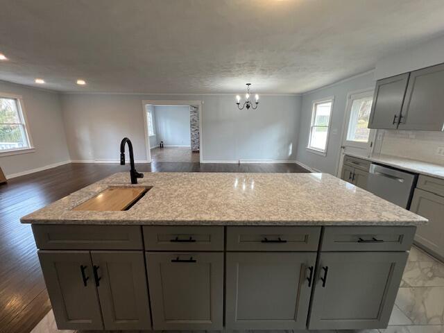 kitchen with stainless steel dishwasher, gray cabinetry, open floor plan, a healthy amount of sunlight, and a sink