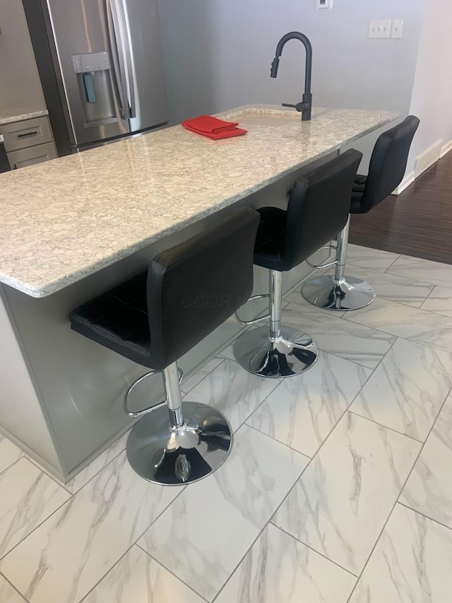 kitchen with marble finish floor, a kitchen bar, stainless steel refrigerator with ice dispenser, and a sink