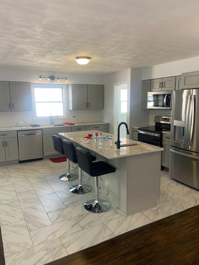 kitchen with marble finish floor, gray cabinets, stainless steel appliances, and a sink