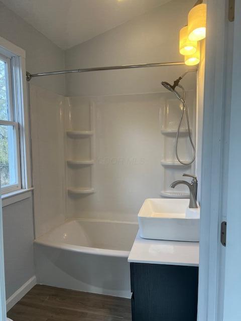 full bath featuring shower / bathtub combination, wood finished floors, vanity, baseboards, and vaulted ceiling