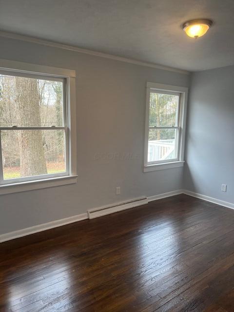 empty room featuring dark wood-style floors, a baseboard radiator, baseboards, and ornamental molding