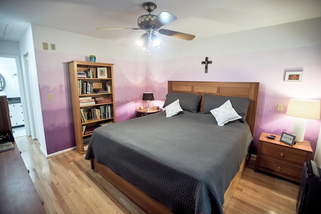 bedroom featuring light wood finished floors, attic access, and ceiling fan