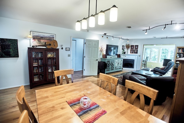 dining room with rail lighting, a fireplace, and wood finished floors