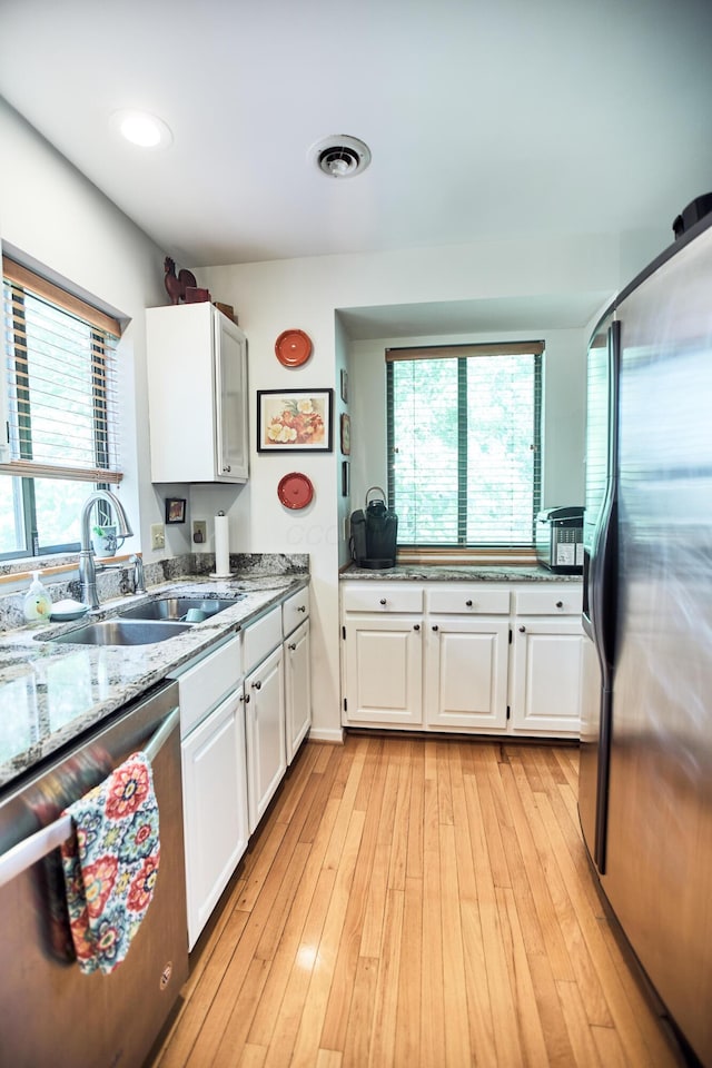 kitchen featuring stainless steel appliances, visible vents, light wood-style flooring, white cabinetry, and a sink