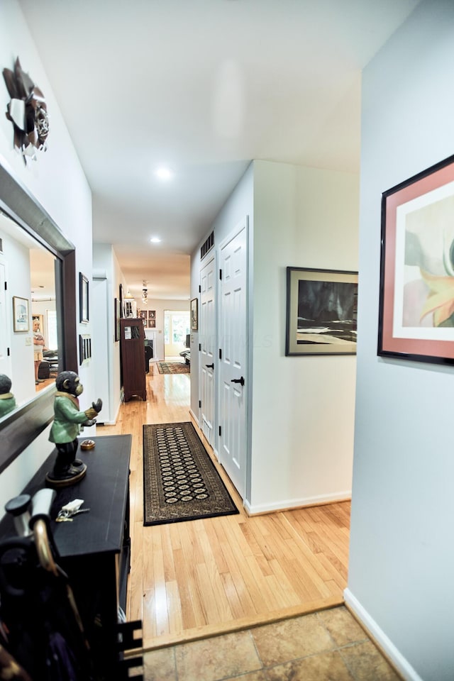 hallway with light wood finished floors, visible vents, and baseboards