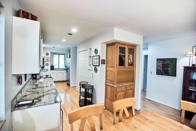 kitchen featuring light stone counters, recessed lighting, light wood-style floors, freestanding refrigerator, and white cabinetry