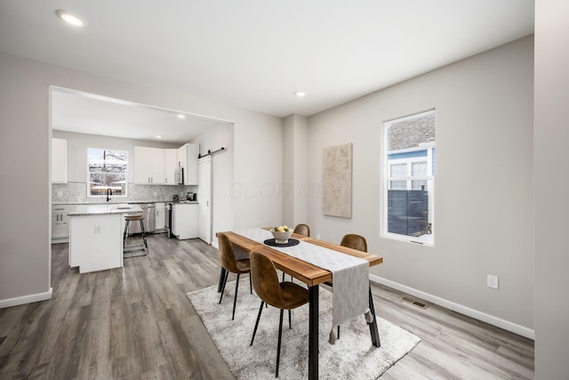 dining space with a barn door, visible vents, light wood-style flooring, and baseboards