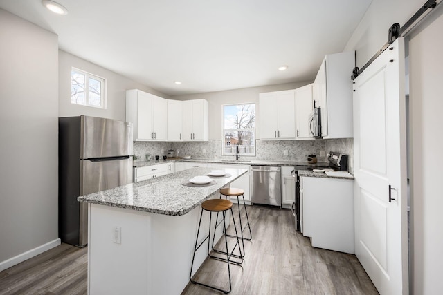 kitchen featuring light stone counters, tasteful backsplash, a barn door, appliances with stainless steel finishes, and a sink