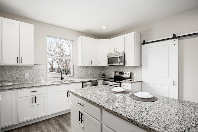 kitchen featuring a barn door, a sink, appliances with stainless steel finishes, light stone countertops, and tasteful backsplash