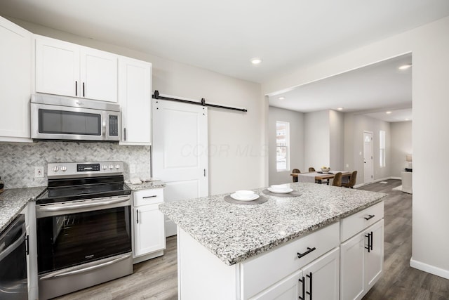 kitchen featuring a barn door, appliances with stainless steel finishes, light wood-type flooring, decorative backsplash, and light stone countertops