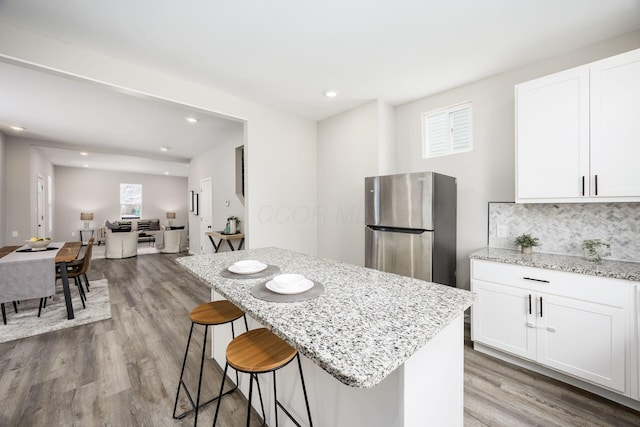 kitchen with tasteful backsplash, light stone counters, a kitchen breakfast bar, wood finished floors, and freestanding refrigerator