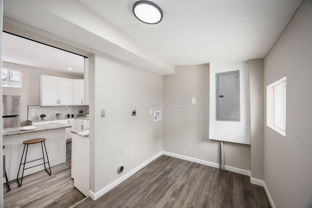 laundry area featuring hookup for a washing machine, electric panel, baseboards, and wood finished floors