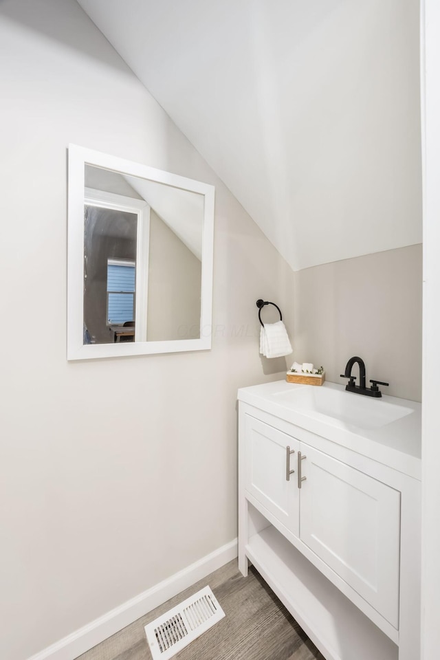 bathroom with baseboards, visible vents, wood finished floors, vaulted ceiling, and vanity