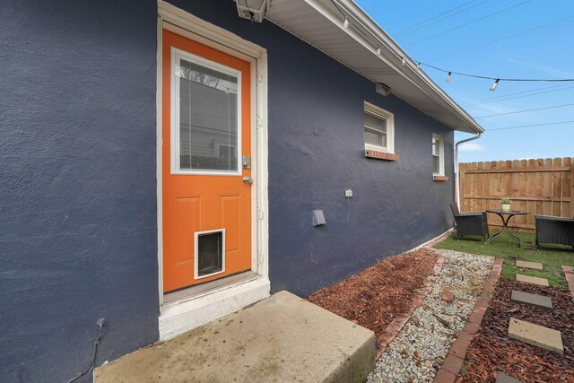 doorway to property with fence and stucco siding