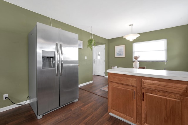 kitchen featuring stainless steel fridge, baseboards, brown cabinetry, dark wood-type flooring, and light countertops