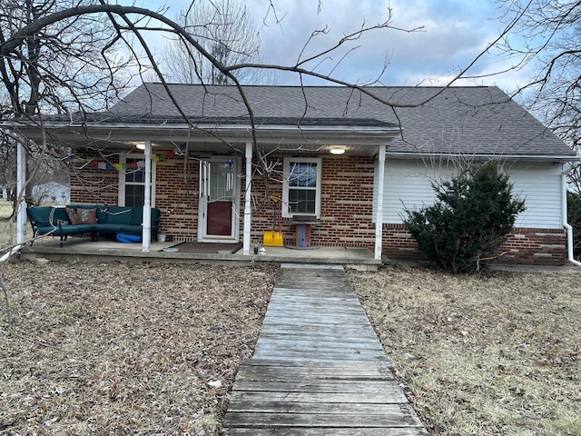 view of front of property with a shingled roof, covered porch, and brick siding