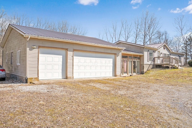 exterior space featuring a garage, metal roof, a wooden deck, and dirt driveway