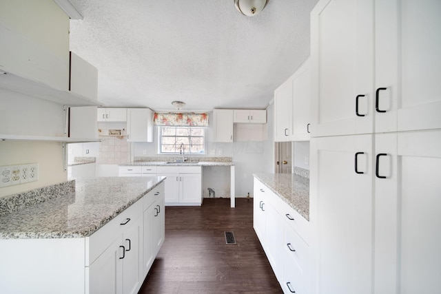 kitchen with light stone counters, a sink, visible vents, tasteful backsplash, and dark wood finished floors