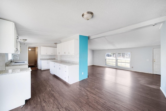 kitchen with white cabinets, open floor plan, dark wood-type flooring, light stone countertops, and a sink