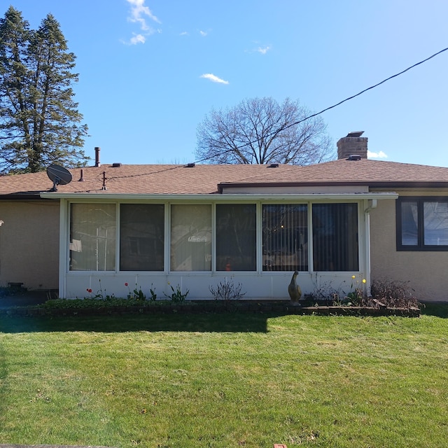 exterior space featuring a shingled roof, a sunroom, a lawn, stucco siding, and a chimney