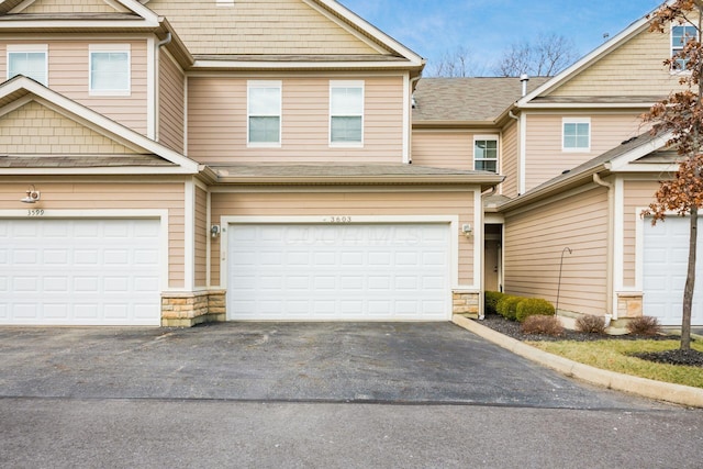 townhome / multi-family property with a garage, stone siding, and driveway