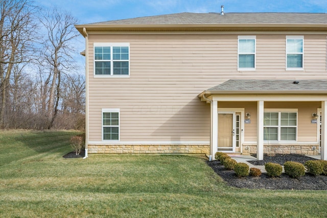 view of front of home with stone siding, roof with shingles, and a front yard