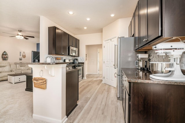 kitchen with a breakfast bar area, stainless steel appliances, tasteful backsplash, open floor plan, and dark brown cabinets