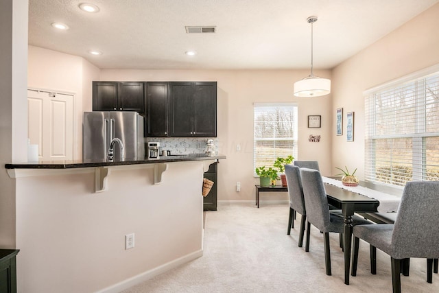 kitchen with a breakfast bar area, high end refrigerator, visible vents, dark cabinetry, and decorative light fixtures