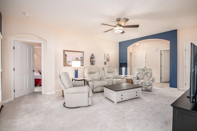 carpeted living area with ceiling fan, arched walkways, and baseboards