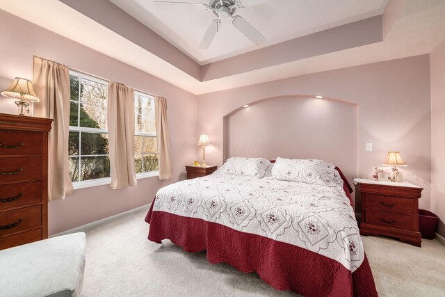 carpeted bedroom with baseboards, a tray ceiling, and a ceiling fan