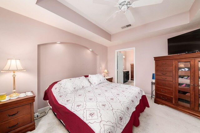 bedroom featuring baseboards, visible vents, a raised ceiling, light colored carpet, and ensuite bath