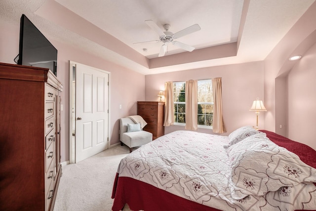 bedroom featuring light carpet, baseboards, a raised ceiling, and a ceiling fan