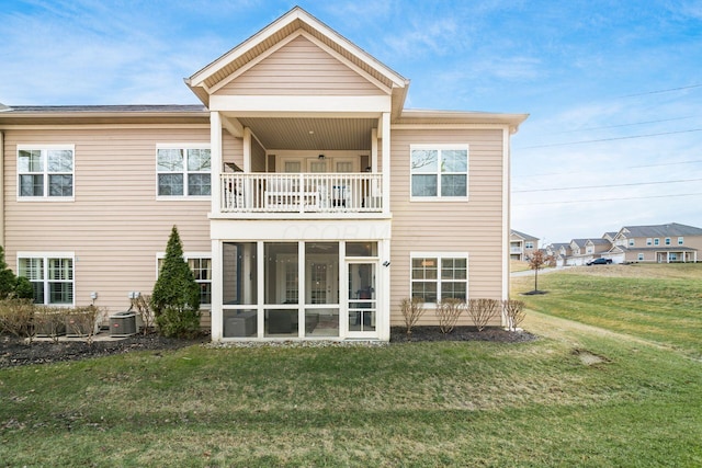 rear view of house with a balcony, a sunroom, central AC, and a lawn