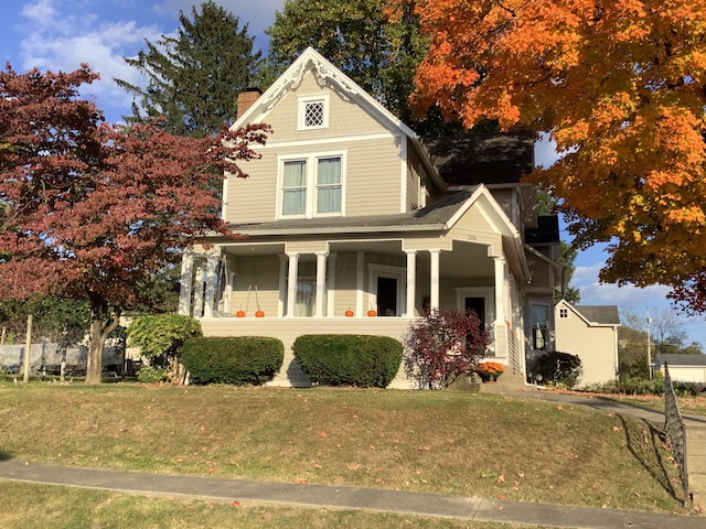 victorian home with covered porch, a front lawn, and a chimney