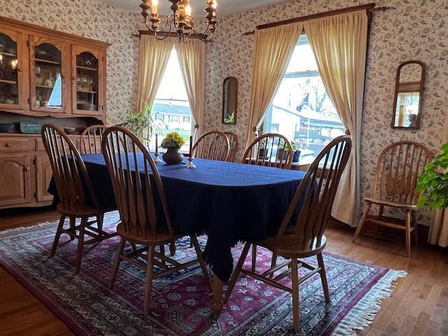 dining area featuring a notable chandelier, wood finished floors, and wallpapered walls