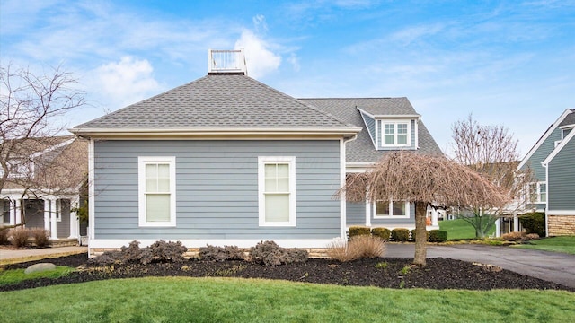 view of side of property with a shingled roof, driveway, and a lawn