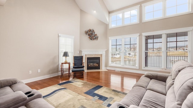 living area with a high ceiling, a fireplace, baseboards, and wood finished floors