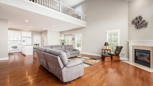 living room with recessed lighting, a high ceiling, a premium fireplace, baseboards, and wood-type flooring