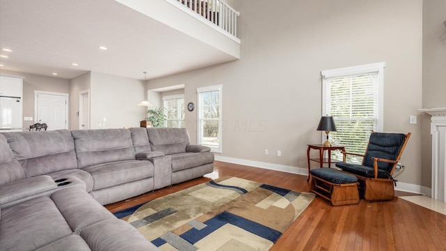 living area featuring baseboards, a towering ceiling, hardwood / wood-style flooring, a premium fireplace, and recessed lighting